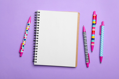 Photo of Open notebook and pens on lilac background, flat lay
