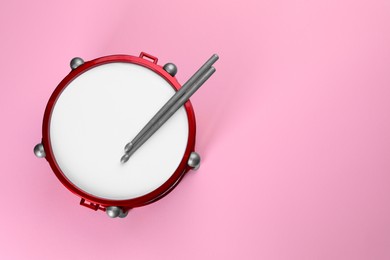 Children's drum with drumsticks on pink background, top view. Space for text