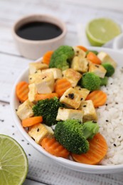 Photo of Bowl of rice with fried tofu, broccoli and carrots on white wooden table, closeup