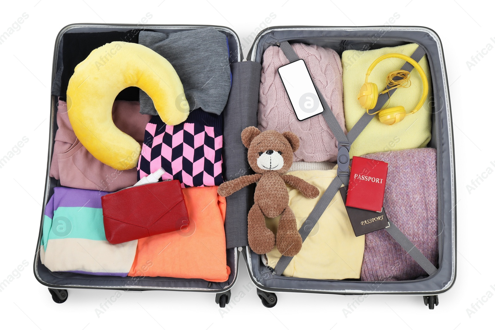 Photo of Soft travel pillow, headphones, passports and other items in open suitcase isolated on white, top view