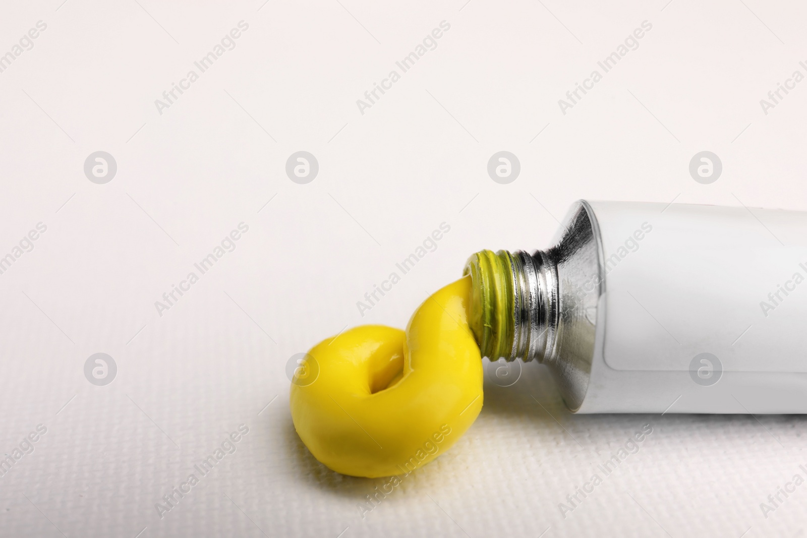 Photo of Tube with yellow oil paint on blank canvas, closeup. Space for text