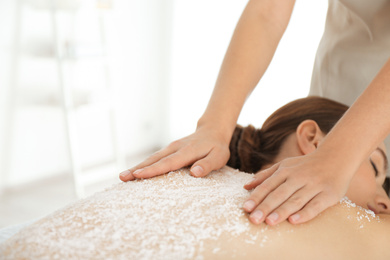 Photo of Young woman having body scrubbing procedure with sea salt in spa salon
