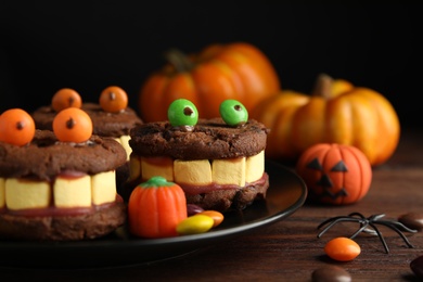 Photo of Delicious desserts decorated as monsters on wooden table, closeup. Halloween treat