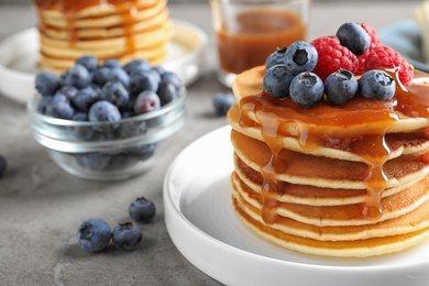 Delicious pancakes with fresh berries and syrup on grey table