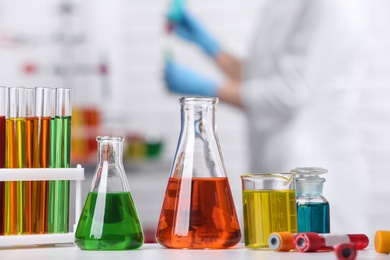 Photo of Different glassware on table and scientist in chemistry laboratory