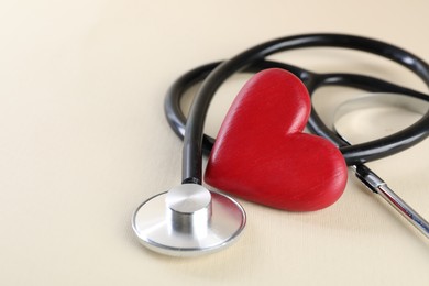 Photo of Stethoscope and red heart on beige background, closeup. Space for text