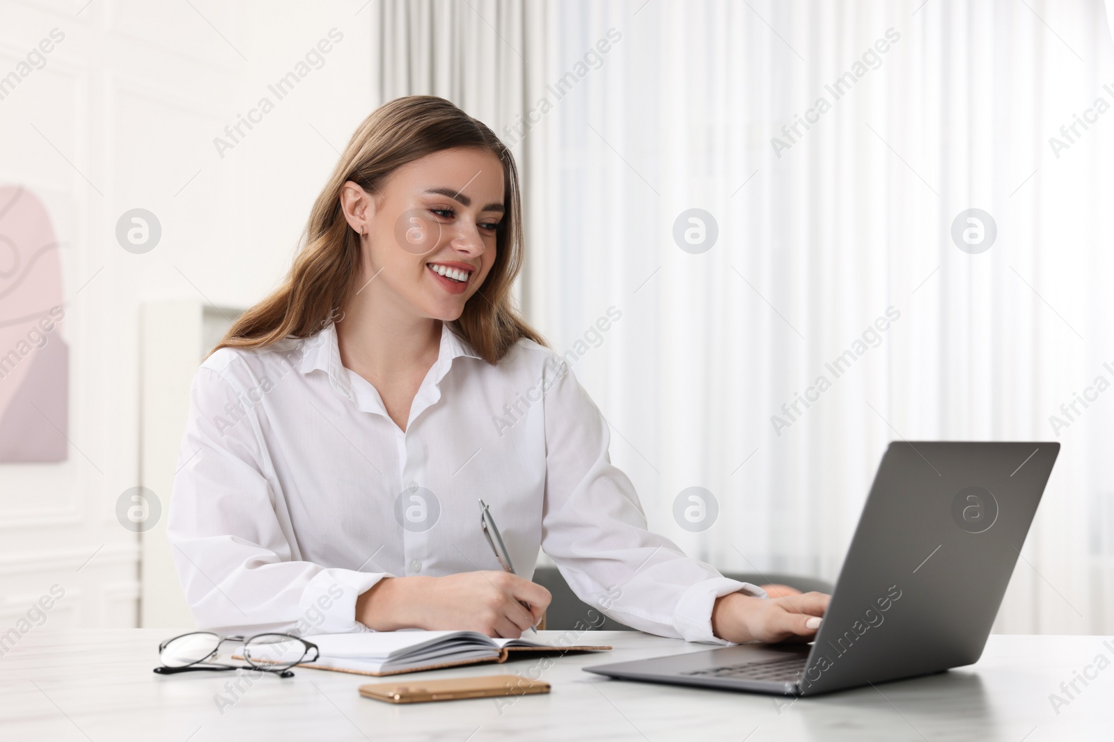 Photo of Happy woman with notebook and laptop at white table in room