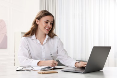 Happy woman with notebook and laptop at white table in room