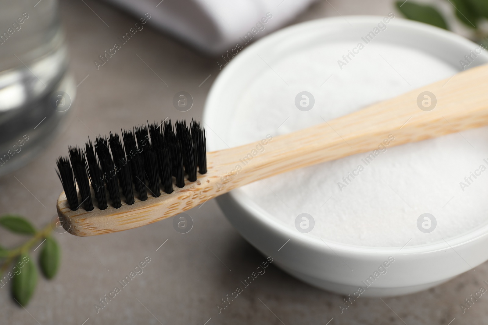 Photo of Bamboo toothbrush and bowl of baking soda on grey table, closeup