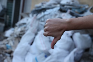 Woman showing thumb down near garbage outdoors, closeup. Space for text