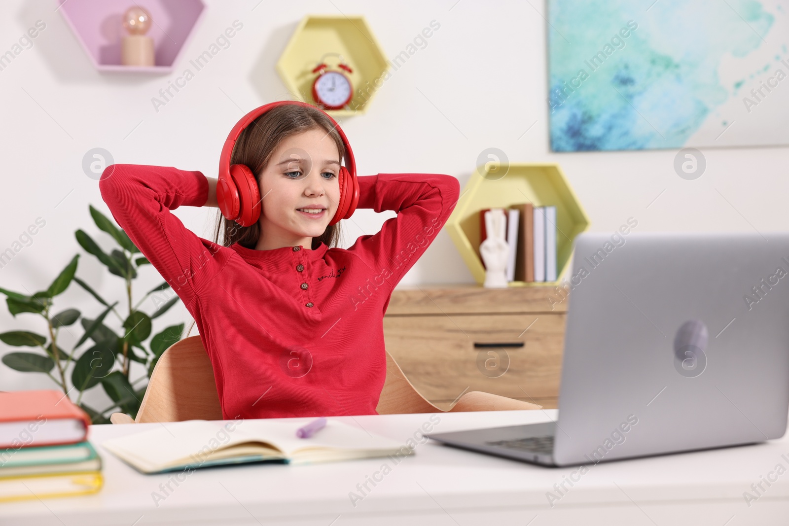 Photo of E-learning. Cute girl using laptop and headphones during online lesson at table indoors