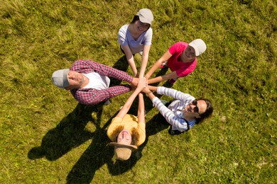 Image of Top aerial view of happy people holding hands together in circle on green grass. Drone photography