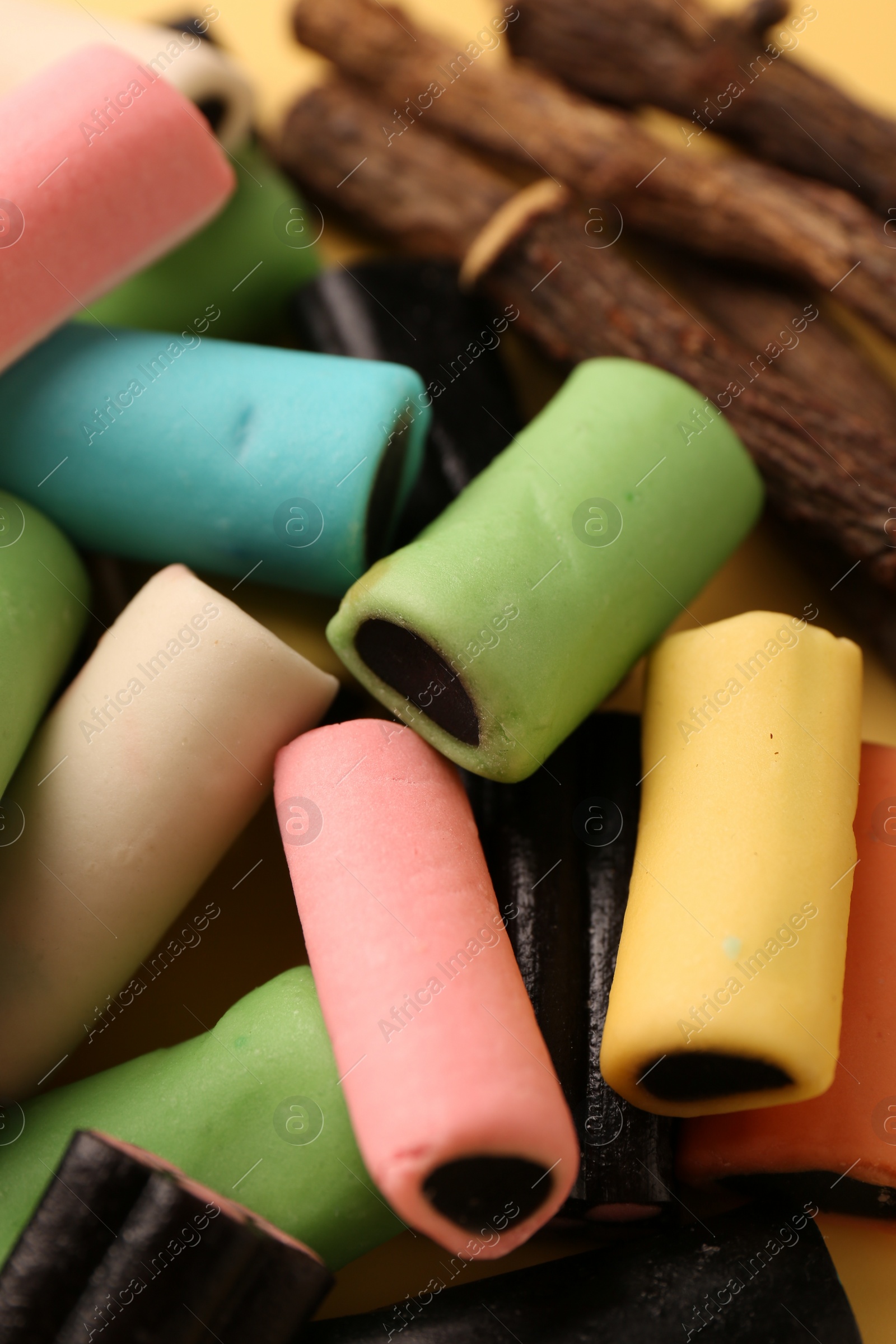 Photo of Tasty candies and dried liquorice roots on yellow background, closeup