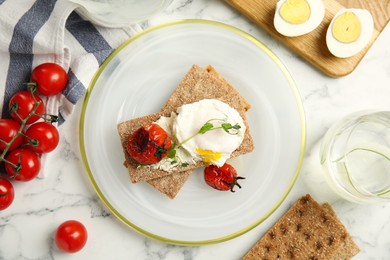 Photo of Fresh rye crispbreads with poached egg, cream cheese and grilled tomatoes on white marble table, flat lay