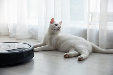 Photo of Modern robotic vacuum cleaner and cute cat on floor indoors