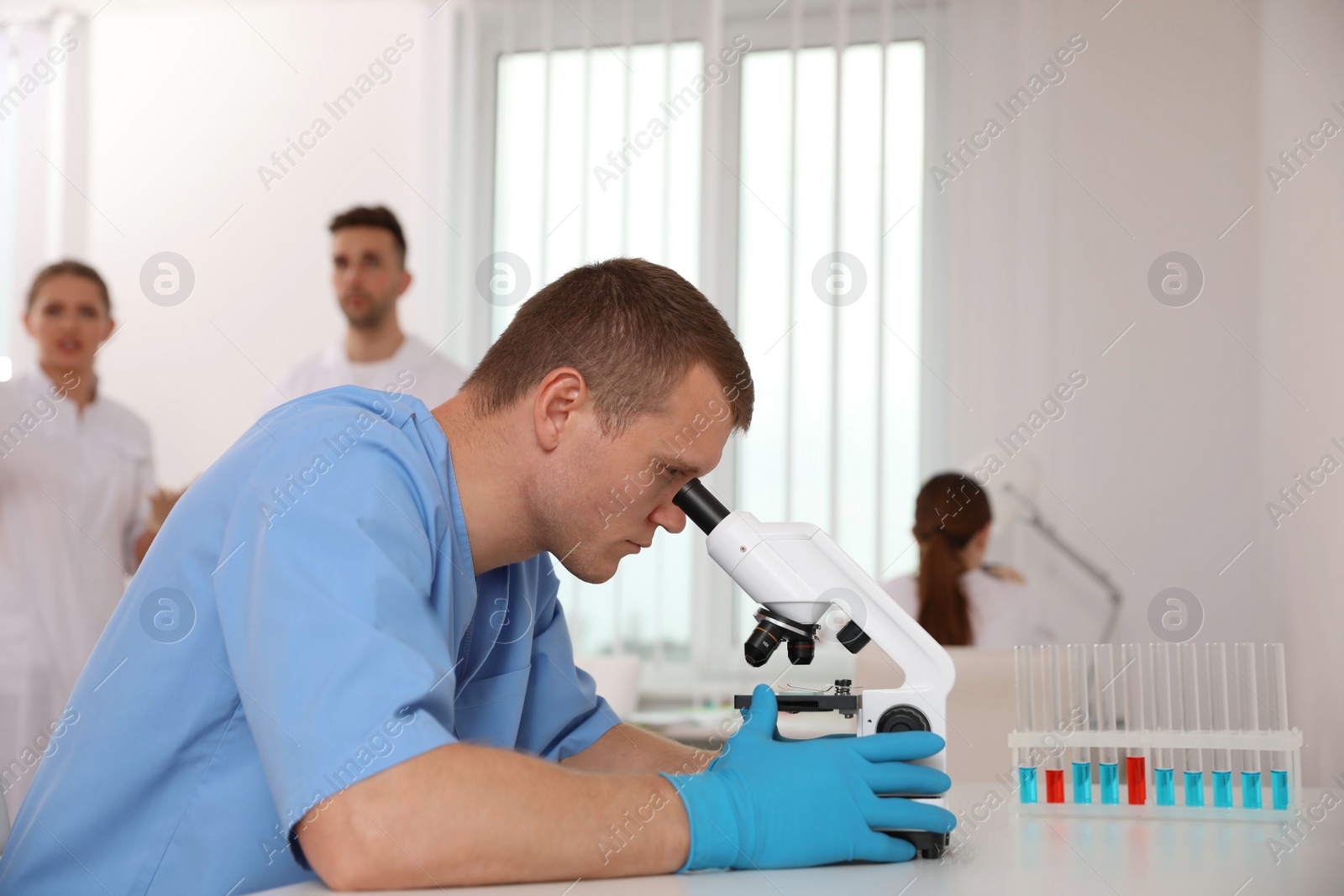 Photo of Scientist using microscope at table and colleagues in laboratory. Medical research