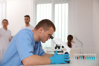 Scientist using microscope at table and colleagues in laboratory. Medical research