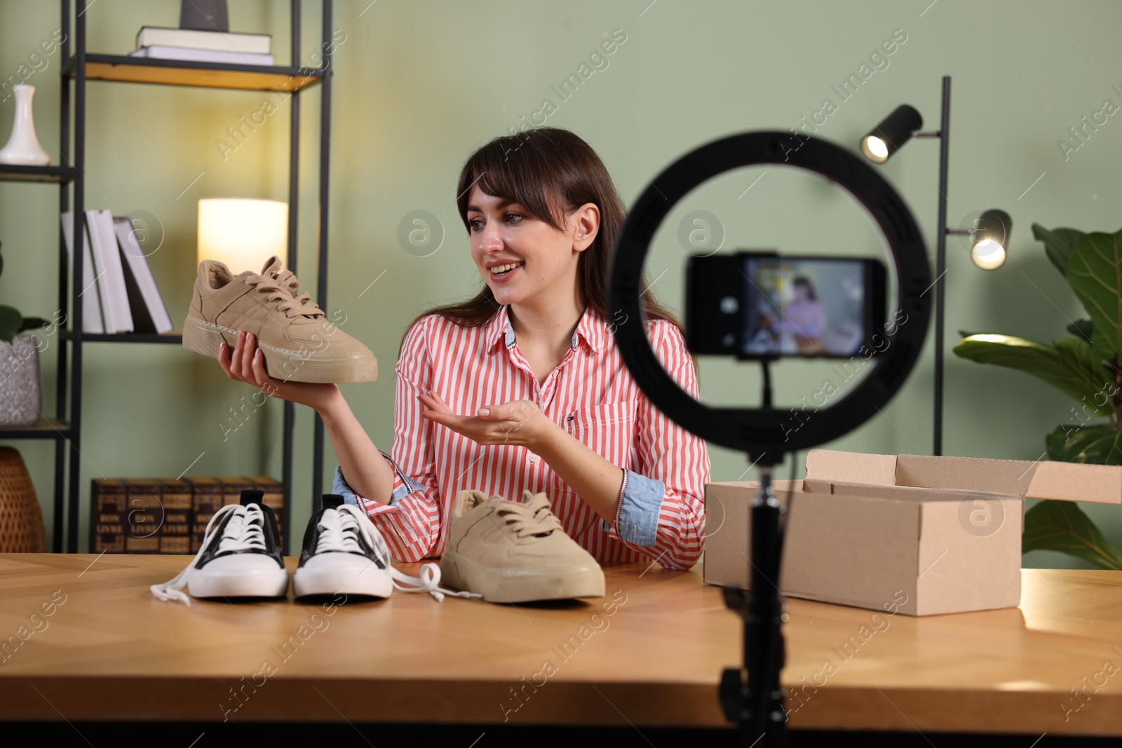 Photo of Smiling fashion blogger recording video while talking about sneakers at home