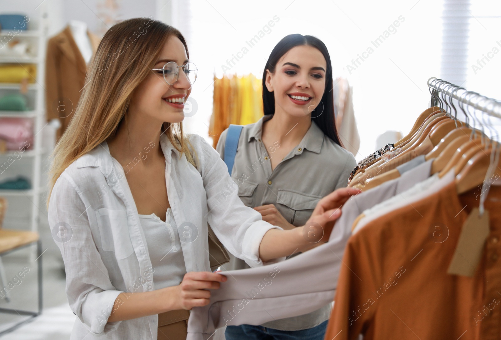 Photo of Young women choosing clothes near rack in modern boutique