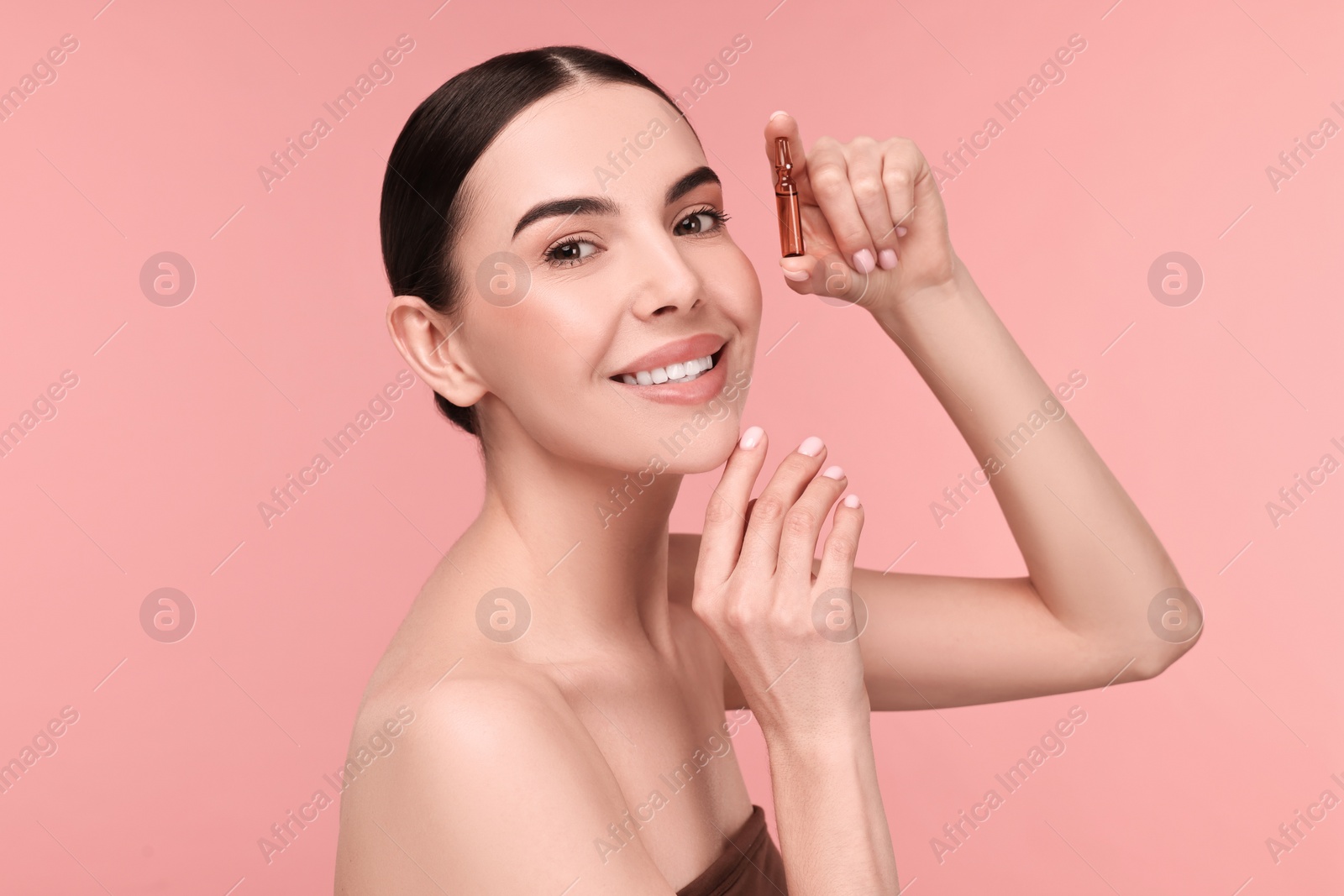 Photo of Beautiful young woman holding skincare ampoule on pink background