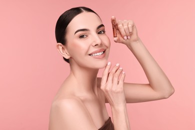 Photo of Beautiful young woman holding skincare ampoule on pink background