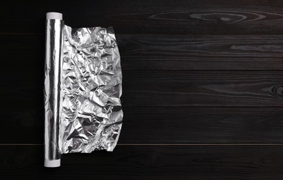 Photo of Roll of aluminum foil on dark wooden table, top view. Space for text