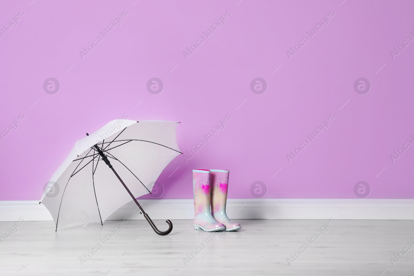 Photo of Beautiful open umbrella and gumboots on floor near color wall with space for design