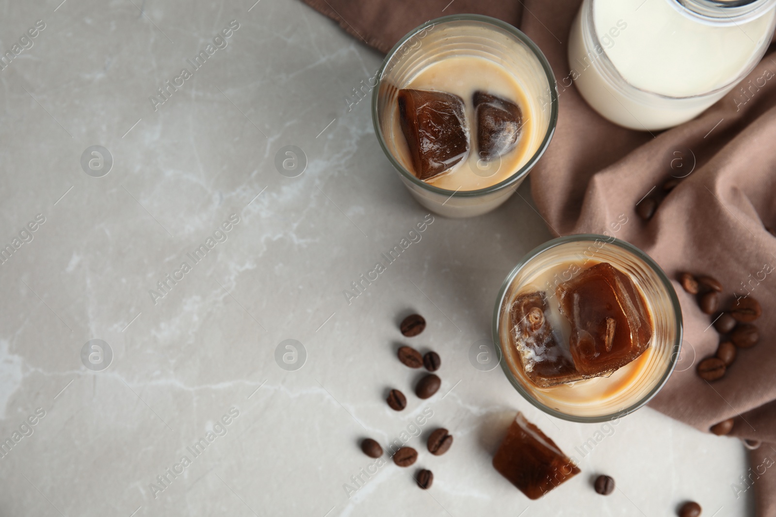 Photo of Glasses of milk with coffee ice cubes on grey table, top view. Space for text