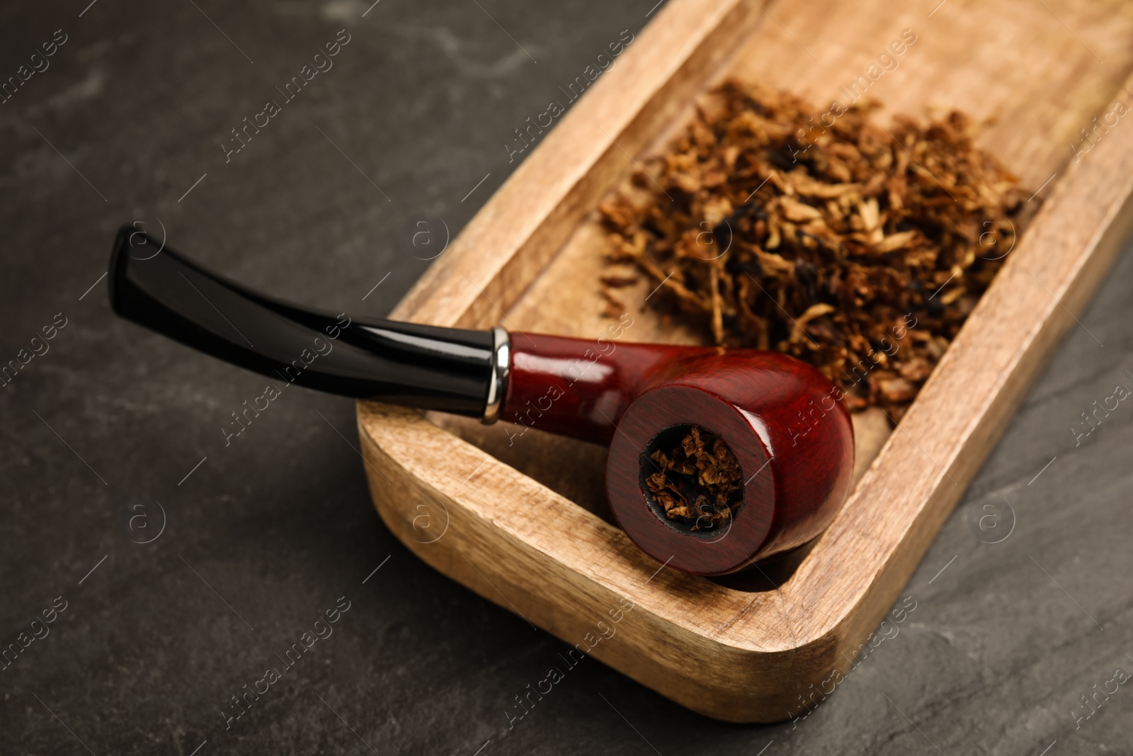 Photo of Tray with smoking pipe and dry tobacco on black table, closeup