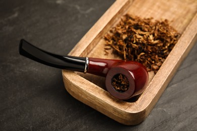 Photo of Tray with smoking pipe and dry tobacco on black table, closeup