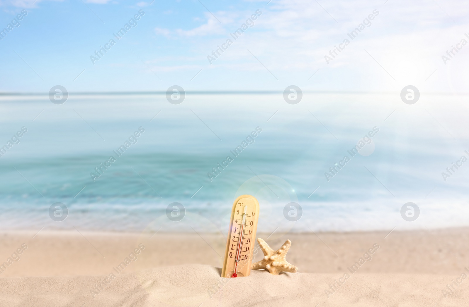 Image of Thermometer, sea star and sandy beach on sunny day