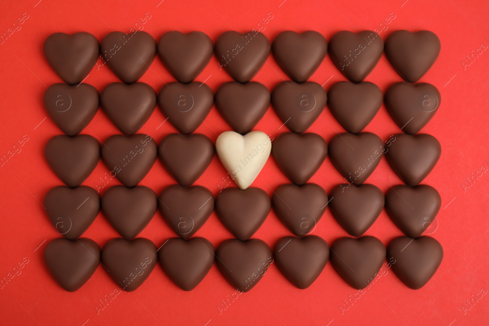 Photo of Tasty heart shaped chocolate candies on red background, flat lay. Happy Valentine's day