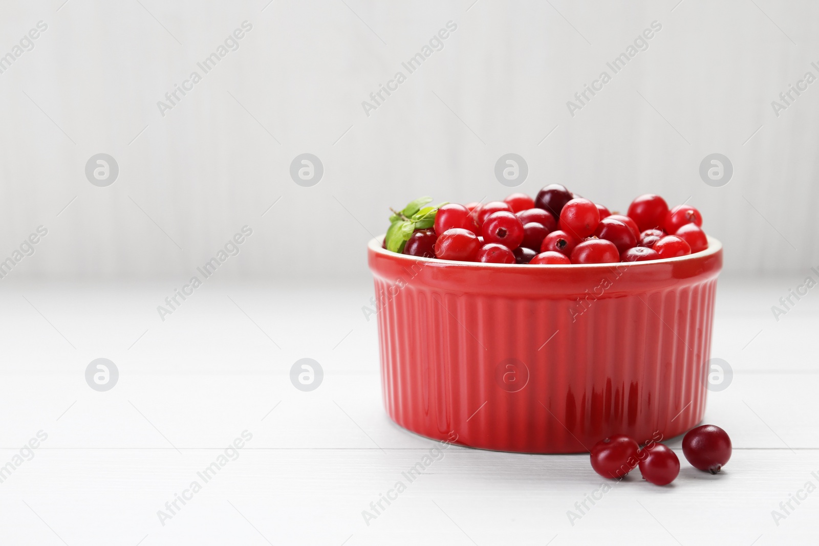 Photo of Fresh ripe cranberries in bowl on white wooden table, closeup. Space for text