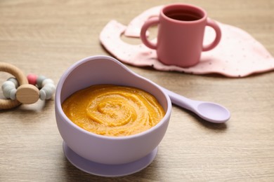 Photo of Plastic dishware with healthy baby food on wooden table. Space for text