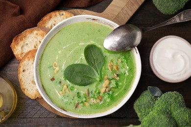 Photo of Delicious broccoli cream soup with basil and pumpkin seeds served on wooden table, flat lay