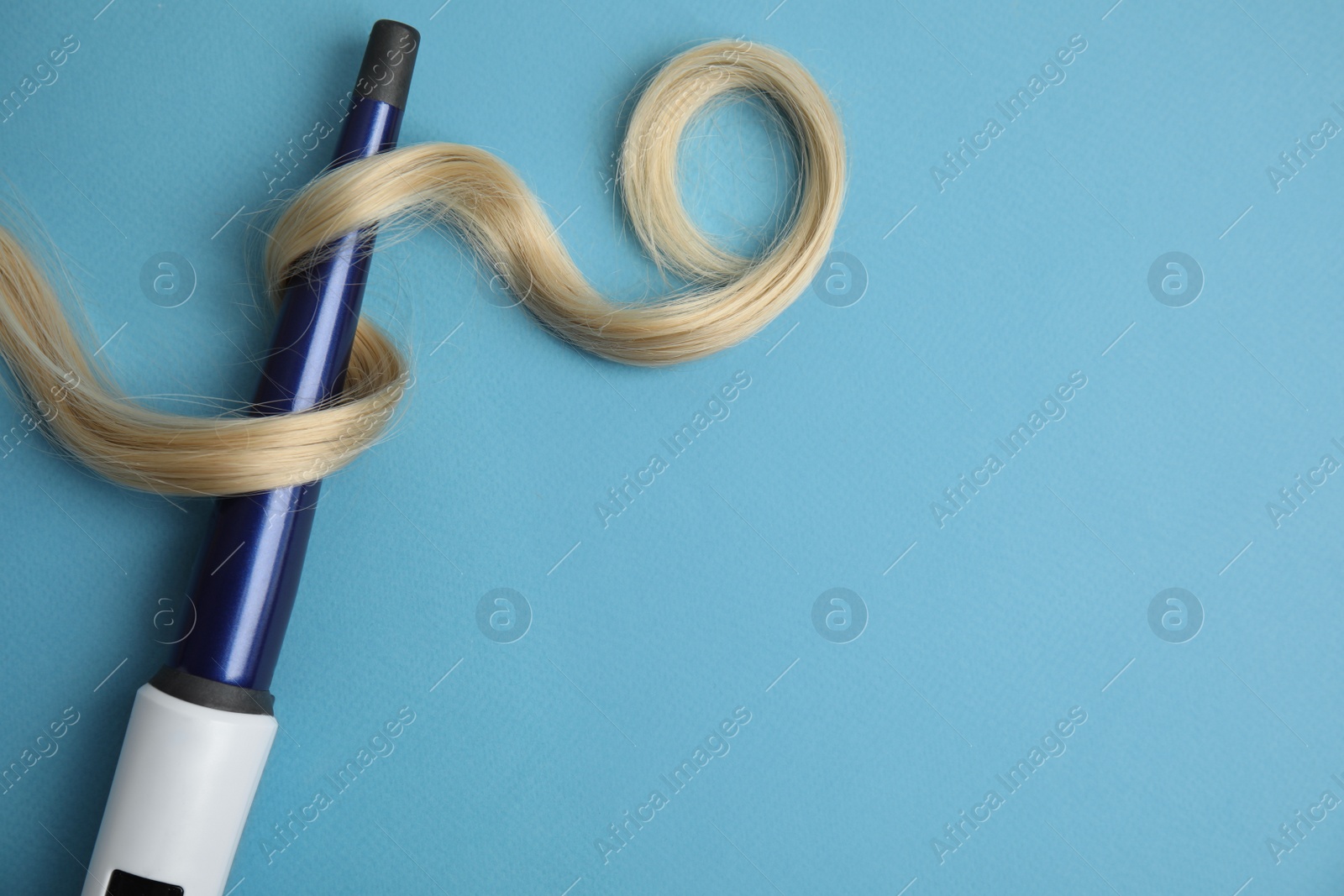 Photo of Curling iron with blonde hair lock on light blue background, flat lay. Space for text