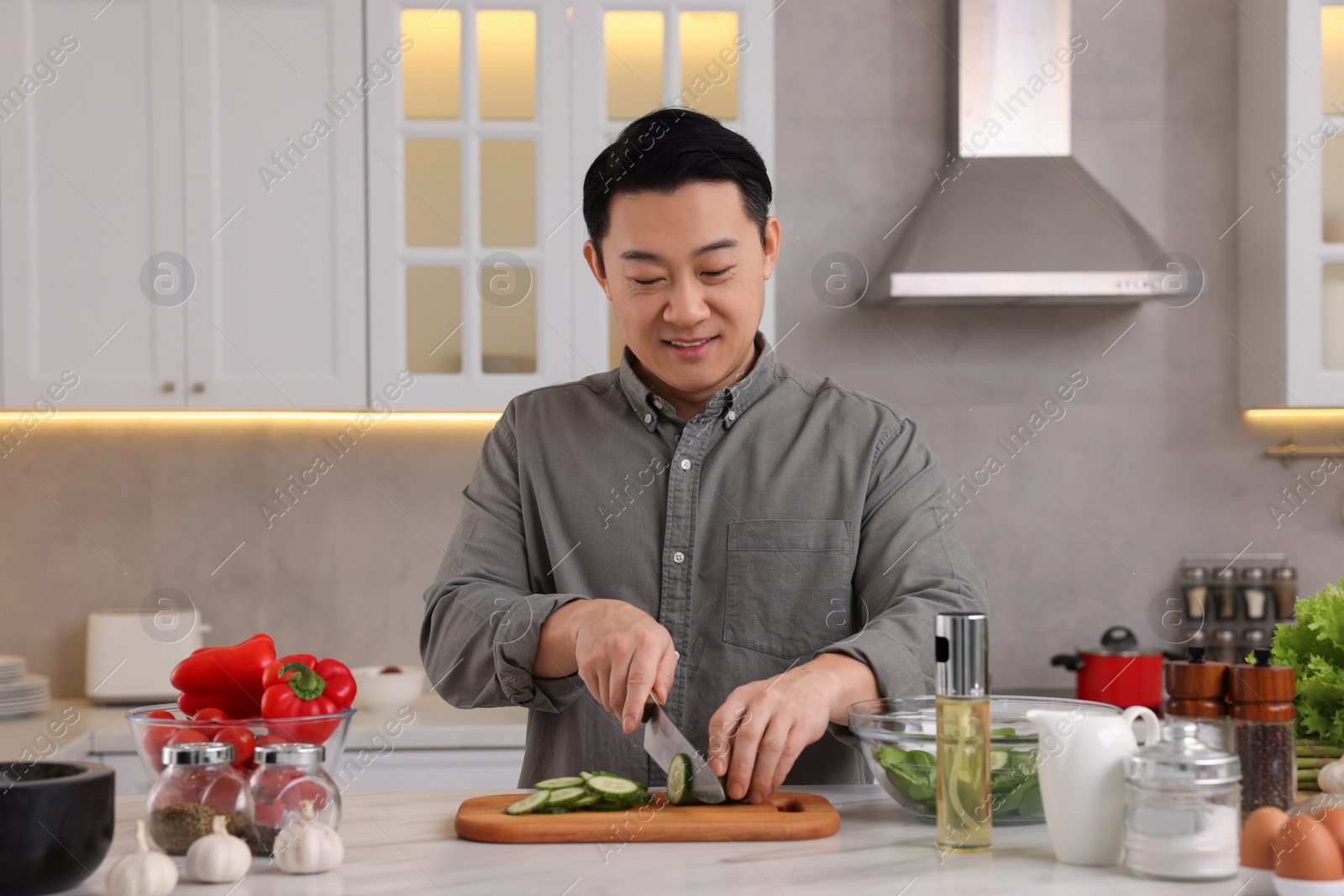 Photo of Cooking process. Man cutting fresh cucumber at countertop in kitchen