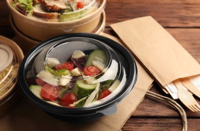 Tasty food in containers with knife and fork on wooden table