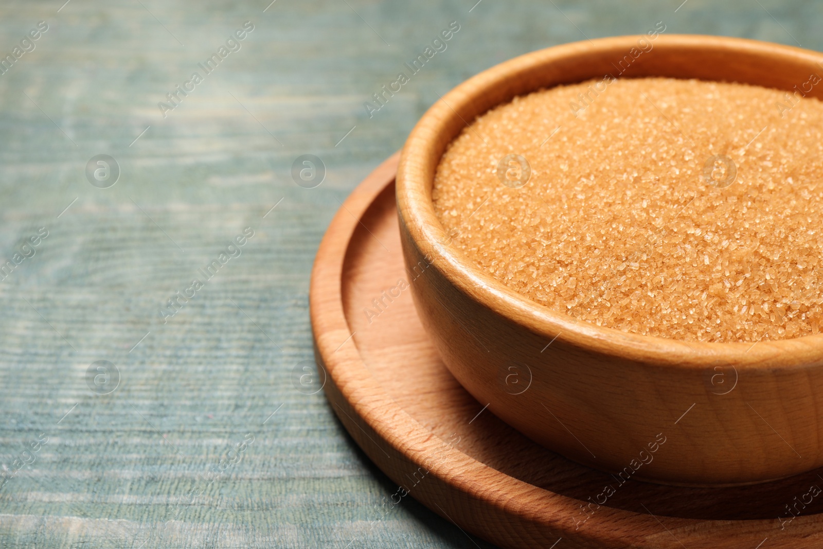 Photo of Brown sugar in bowl on light blue wooden table, closeup. Space for text