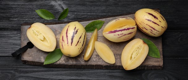 Image of Whole and cut pepino melons with green leaves on black wooden table, top view. Banner design