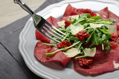 Photo of Eating tasty bresaola salad with fork at table, closeup