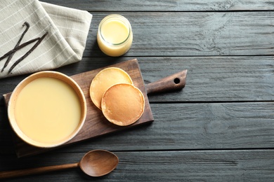 Photo of Bowl of condensed milk and pancakes served on wooden table, top view with space for text. Dairy products