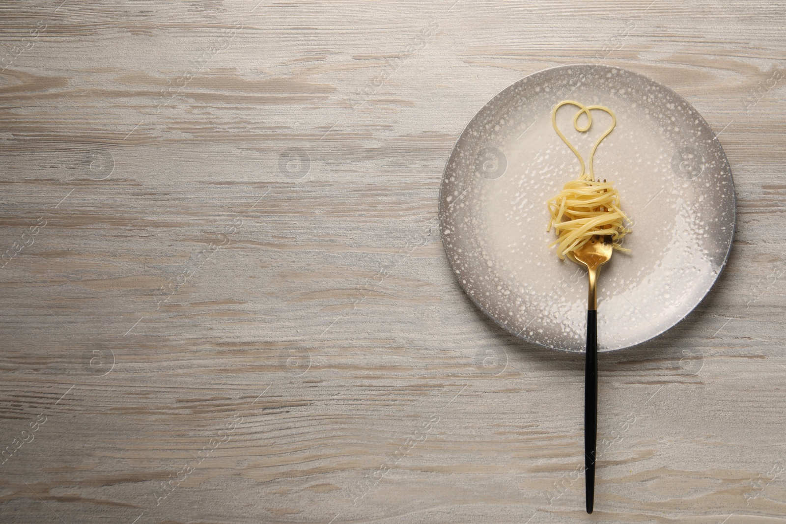 Photo of Heart made with spaghetti and fork on light wooden table, top view. Space for text