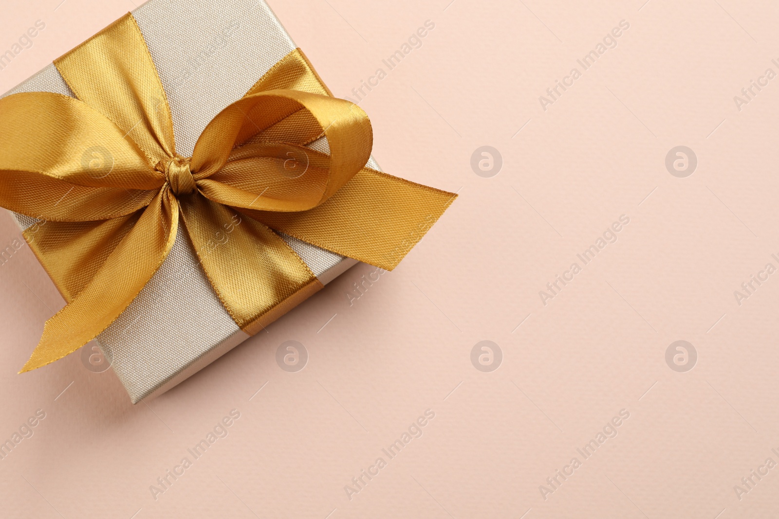 Photo of Beautiful gift box with golden bow on pink background, top view. Space for text