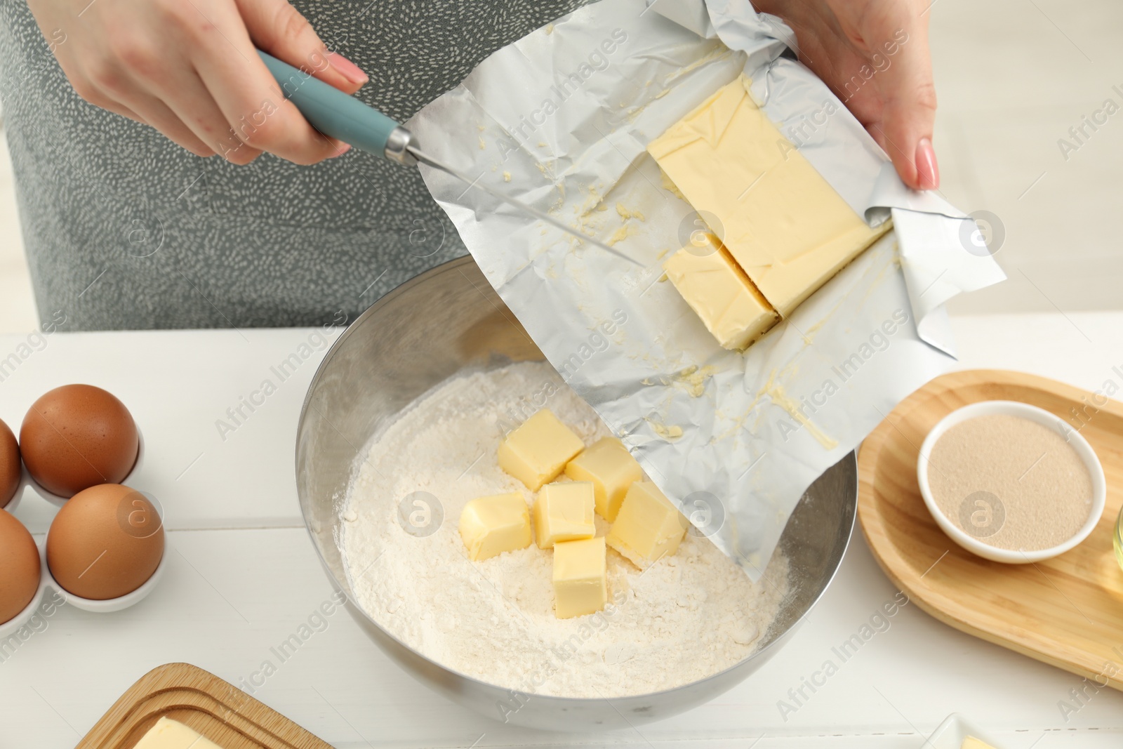 Photo of Woman adding fresh butter into bowl with flour at white wooden table, closeup