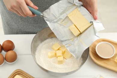 Photo of Woman adding fresh butter into bowl with flour at white wooden table, closeup