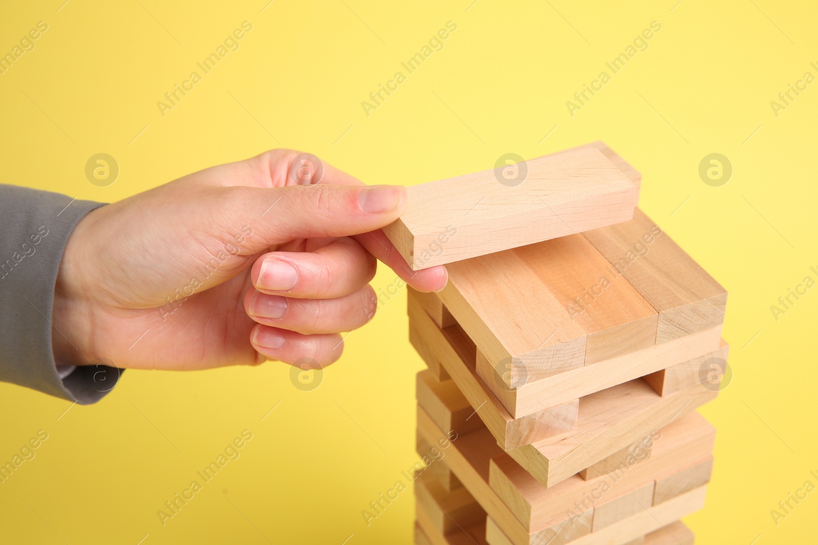 Photo of Woman playing Jenga tower on yellow background, closeup