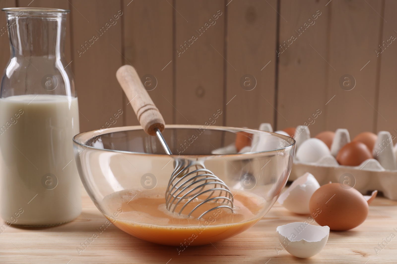 Photo of Making dough. Beaten eggs in bowl, shells and milk on wooden table, closeup