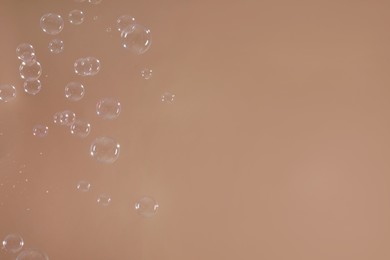 Many beautiful soap bubbles on light brown background. Space for text