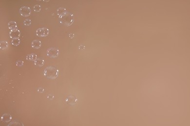 Photo of Many beautiful soap bubbles on light brown background. Space for text